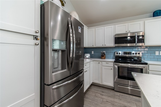 kitchen featuring white cabinetry, stainless steel appliances, light hardwood / wood-style floors, and backsplash