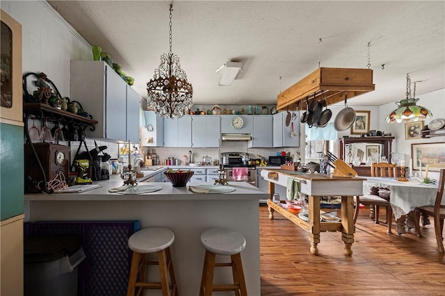 kitchen with decorative light fixtures, light hardwood / wood-style floors, stainless steel electric range, and kitchen peninsula