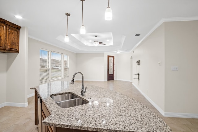 kitchen with ornamental molding, a center island with sink, sink, and light stone counters