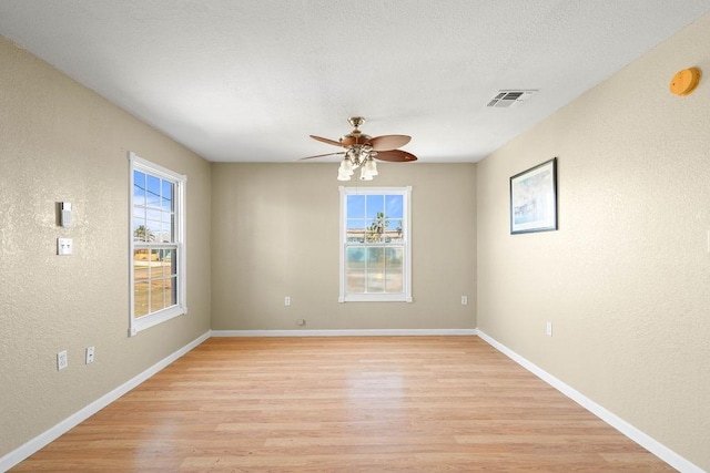 empty room with a healthy amount of sunlight, visible vents, a textured wall, and light wood finished floors