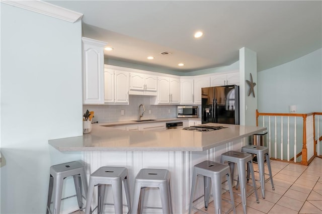 103 E Palmetto Dr Unit B, South Padre Island, TX 78597 - kitchen featuring black fridge with ice dispenser, stainless steel microwave, decorative backsplash, a peninsula, and a breakfast bar