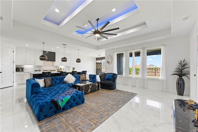 living room with ceiling fan with notable chandelier and a tray ceiling