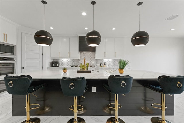 kitchen featuring white cabinets, a kitchen breakfast bar, appliances with stainless steel finishes, and hanging light fixtures