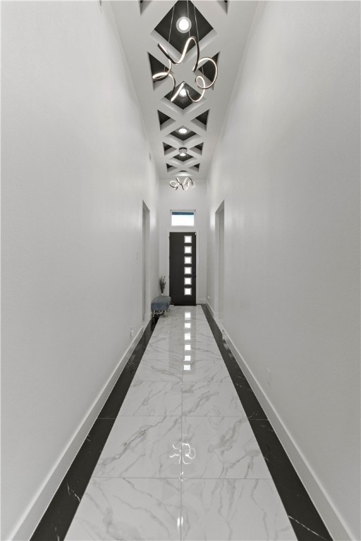 corridor with a notable chandelier, a high ceiling, and coffered ceiling