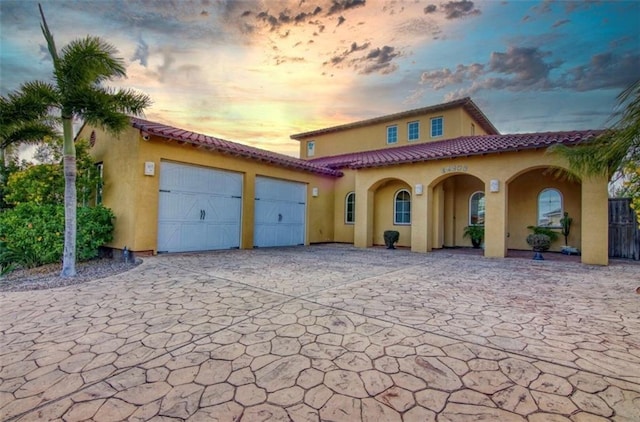 mediterranean / spanish house with a tiled roof, an attached garage, and stucco siding