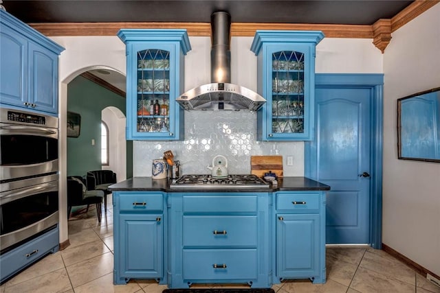 kitchen featuring appliances with stainless steel finishes, wall chimney range hood, decorative backsplash, blue cabinetry, and crown molding