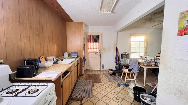 kitchen with a textured ceiling, white gas range, wood walls, and sink