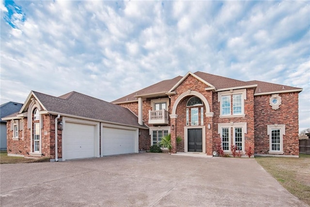 traditional-style house featuring brick siding, a balcony, driveway, and a garage