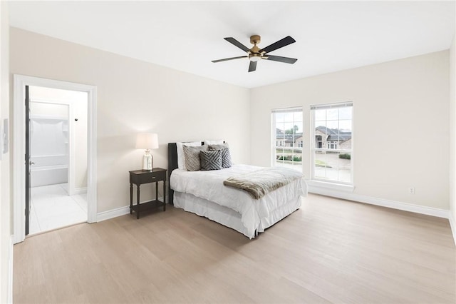 bedroom featuring ceiling fan, ensuite bath, light wood-type flooring, and baseboards