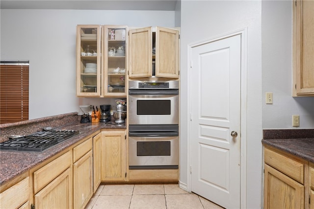 kitchen with dark stone counters, light brown cabinets, light tile patterned floors, and stainless steel appliances