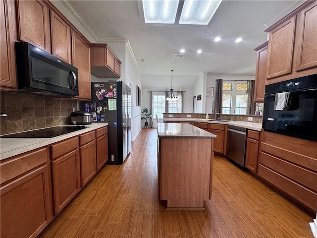 kitchen featuring a peninsula, brown cabinetry, light wood-style flooring, and black appliances