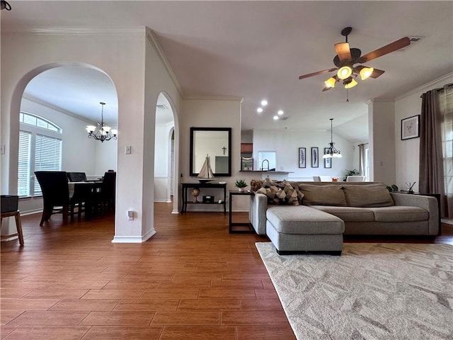 living area with arched walkways, ceiling fan with notable chandelier, wood finished floors, and ornamental molding
