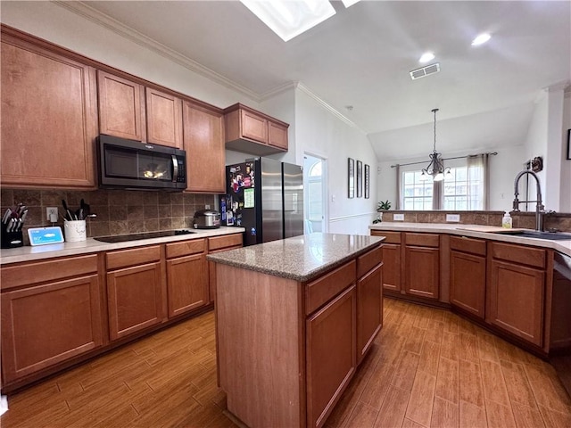 kitchen featuring visible vents, freestanding refrigerator, black electric cooktop, brown cabinets, and a sink