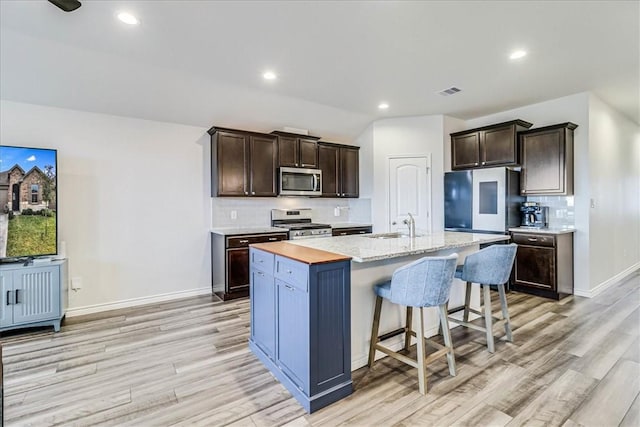 kitchen featuring stainless steel appliances, light hardwood / wood-style floors, a center island with sink, and dark brown cabinetry