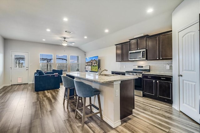 kitchen featuring ceiling fan, vaulted ceiling, a kitchen island with sink, appliances with stainless steel finishes, and a kitchen breakfast bar