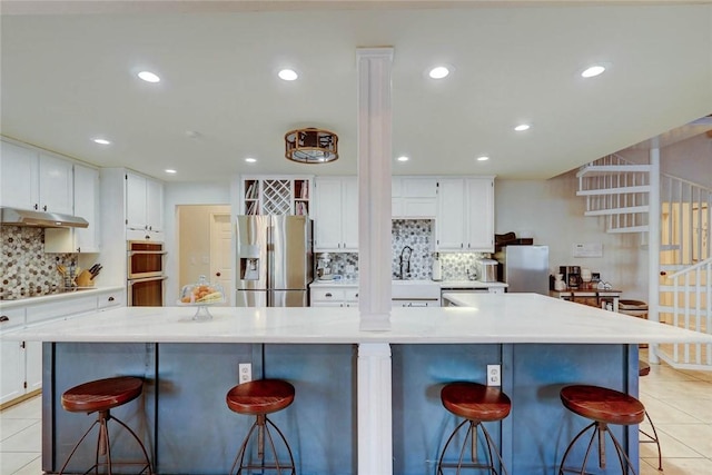 4409 Sue Cir, Corpus Christi, TX 78410 - kitchen with light tile patterned floors, white cabinets, under cabinet range hood, stainless steel appliances, and decorative backsplash