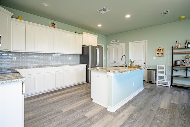 kitchen featuring light hardwood / wood-style floors, stainless steel fridge, a center island with sink, and white cabinetry