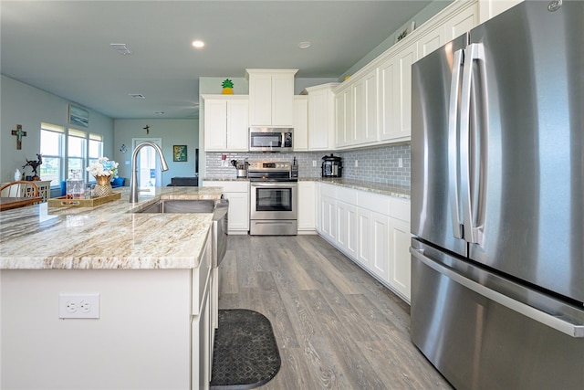 kitchen featuring stainless steel appliances, wood-type flooring, white cabinets, backsplash, and light stone countertops