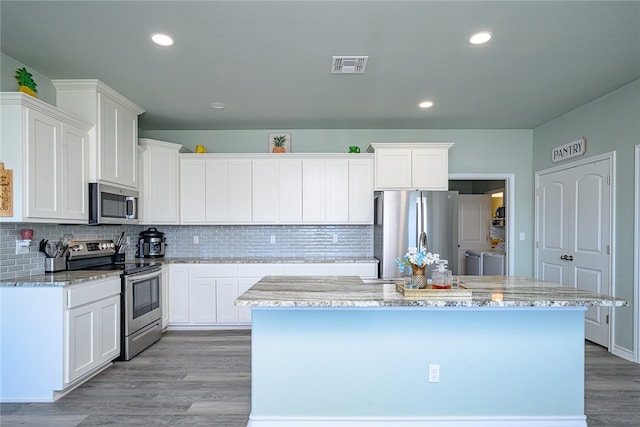 kitchen with light wood-type flooring, appliances with stainless steel finishes, a center island with sink, and white cabinets