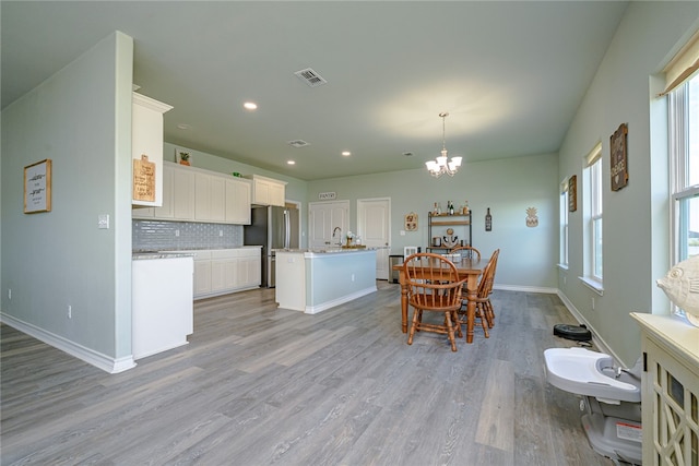 kitchen with a center island with sink, stainless steel fridge, pendant lighting, light hardwood / wood-style floors, and white cabinets