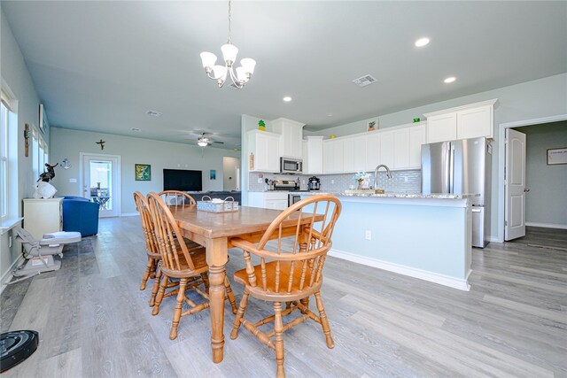 dining space with ceiling fan with notable chandelier, sink, and light wood-type flooring