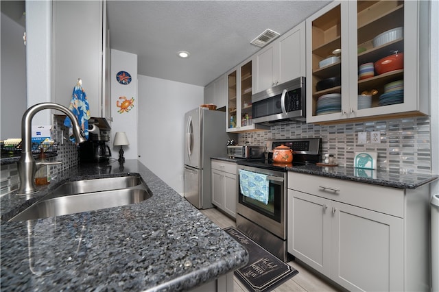 kitchen with sink, appliances with stainless steel finishes, dark stone countertops, white cabinets, and decorative backsplash