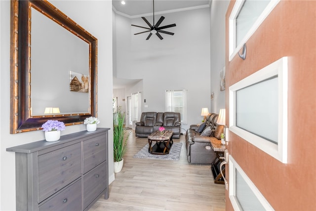 interior space featuring a high ceiling, ornamental molding, ceiling fan, and light hardwood / wood-style flooring