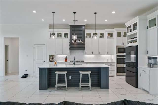 kitchen featuring white cabinetry, appliances with stainless steel finishes, decorative light fixtures, and an island with sink