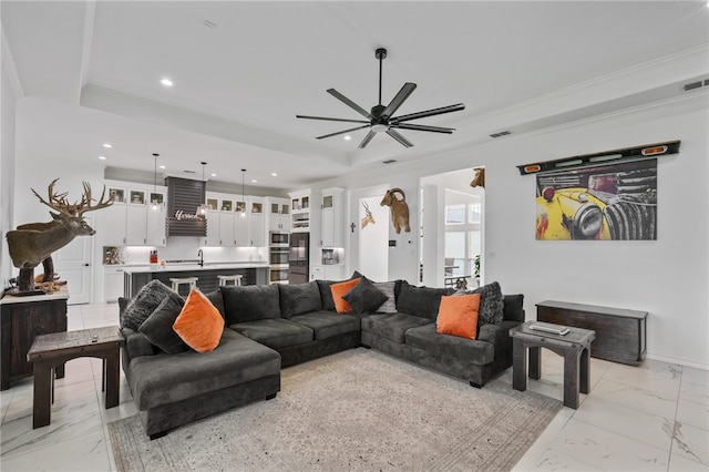 living room with ornamental molding, sink, ceiling fan, and a tray ceiling