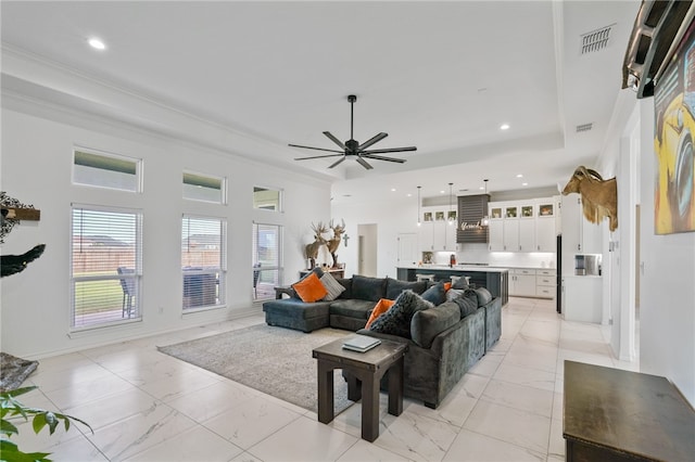 living room with ceiling fan, a raised ceiling, and crown molding