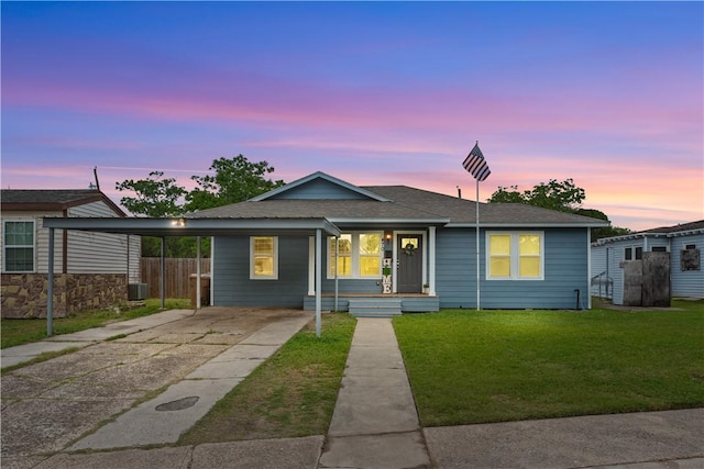bungalow-style house featuring central AC, driveway, a carport, a shingled roof, and a yard