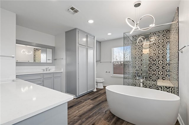 full bathroom with visible vents, toilet, a soaking tub, wood finished floors, and vanity