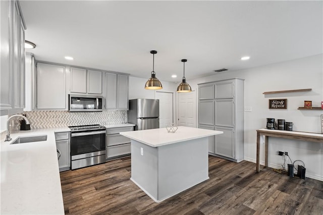 kitchen featuring stainless steel appliances, gray cabinets, light countertops, a sink, and a kitchen island