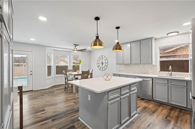 kitchen featuring a center island, light countertops, stainless steel dishwasher, pendant lighting, and a sink