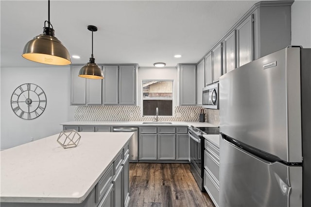 kitchen featuring hanging light fixtures, stainless steel appliances, light countertops, gray cabinetry, and a sink