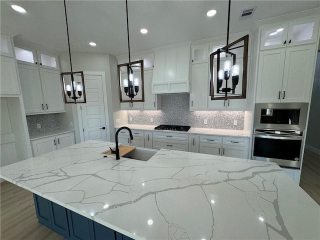 kitchen featuring a center island with sink, sink, hanging light fixtures, light stone countertops, and stainless steel appliances