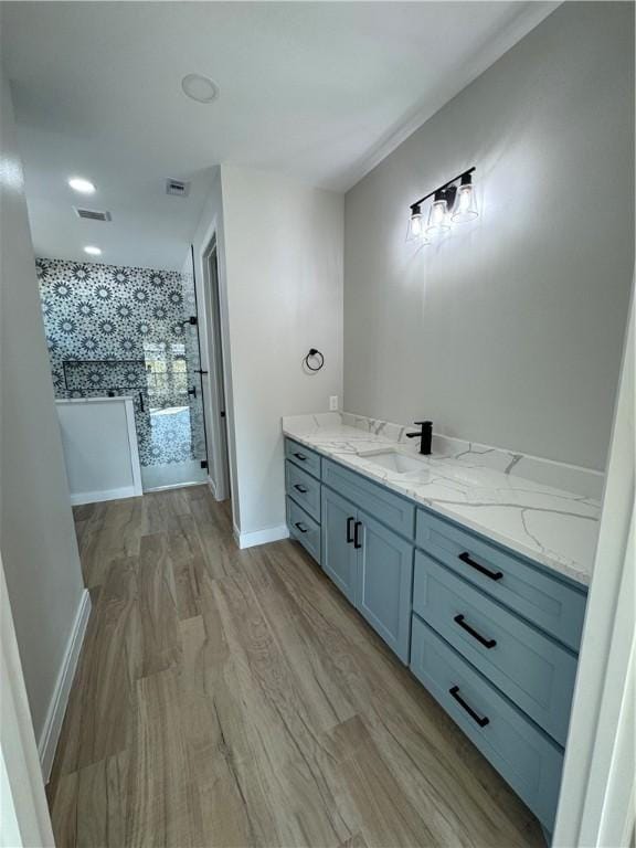 full bathroom featuring baseboards, visible vents, wood finished floors, a tile shower, and vanity