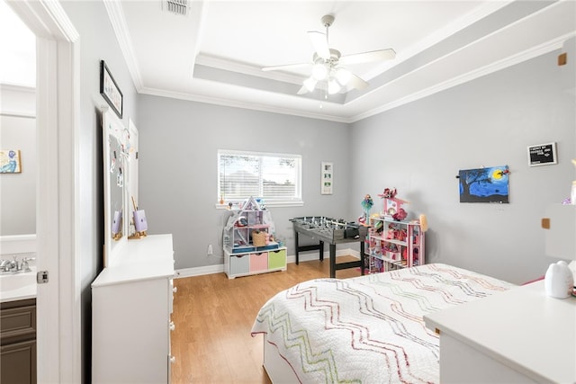 bedroom with crown molding, light wood-type flooring, sink, a tray ceiling, and ceiling fan