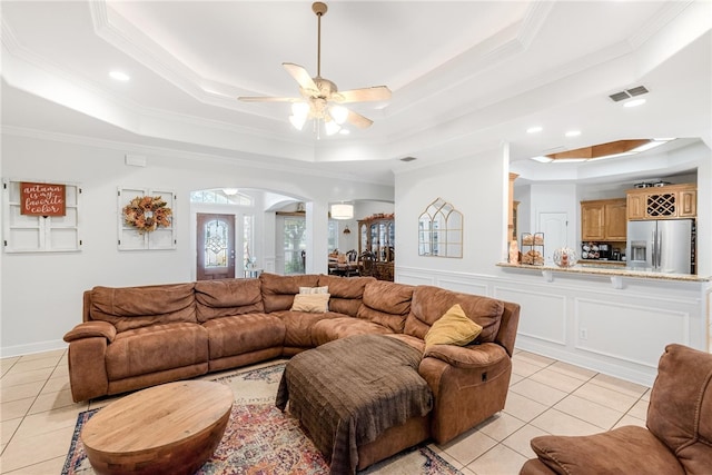 tiled living room featuring ceiling fan, ornamental molding, and a tray ceiling