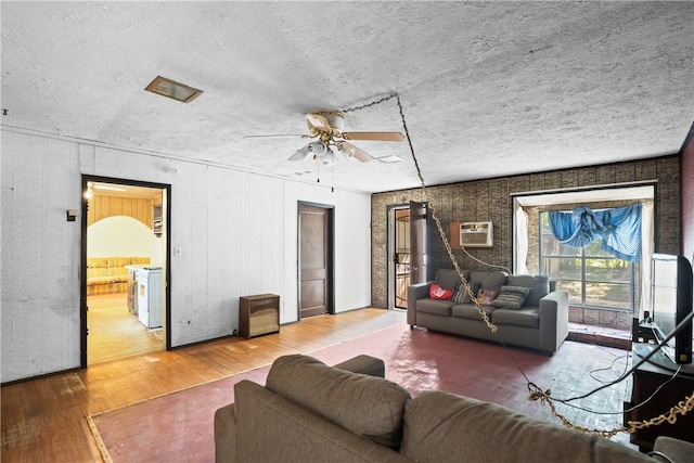 living room with a wall unit AC, hardwood / wood-style flooring, ceiling fan, and a textured ceiling