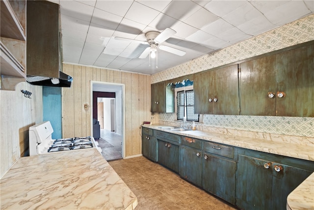 kitchen featuring range hood, dark brown cabinetry, wooden walls, sink, and gas range gas stove