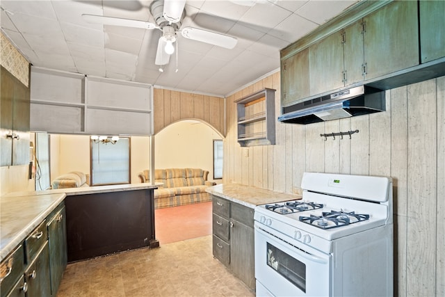 kitchen with white range with gas stovetop, range hood, wood walls, and ceiling fan with notable chandelier