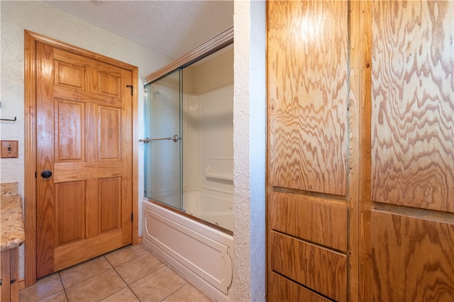 bathroom with bath / shower combo with glass door, a textured ceiling, and tile patterned flooring