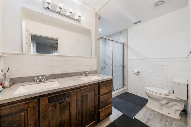 bathroom with vanity, toilet, a shower with shower door, and tile walls