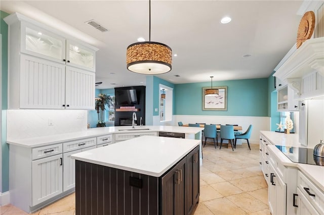 kitchen with white cabinetry, kitchen peninsula, black electric stovetop, a kitchen island, and sink