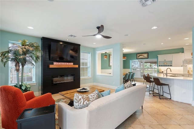 living room with ceiling fan, light tile patterned floors, a large fireplace, and sink