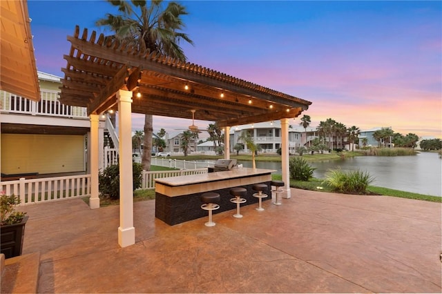 patio terrace at dusk featuring a pergola, a water view, and an outdoor bar