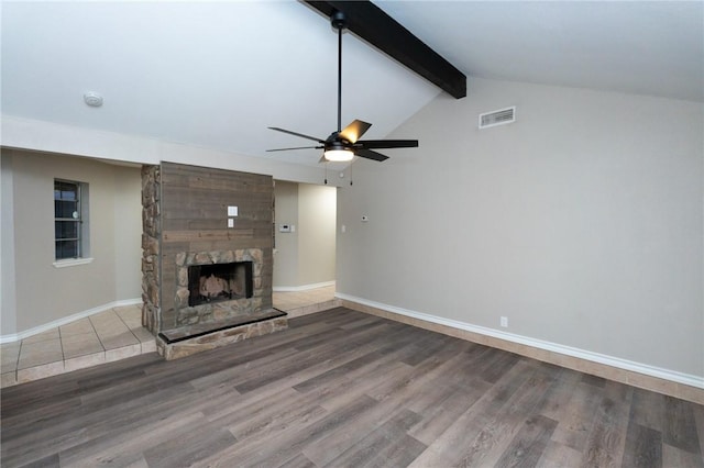 unfurnished living room with hardwood / wood-style floors, vaulted ceiling with beams, ceiling fan, and a stone fireplace