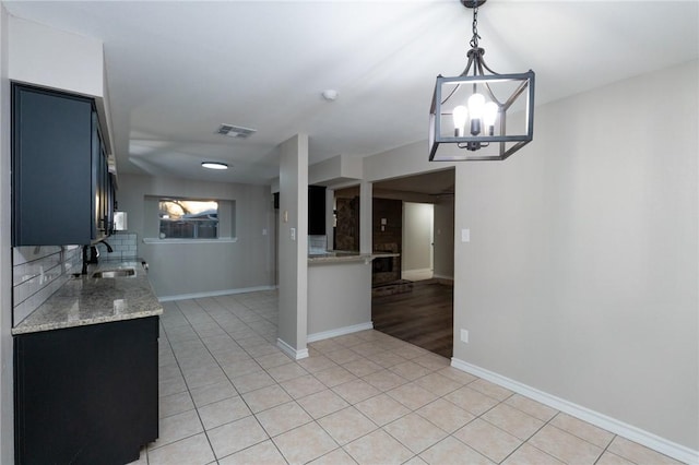 kitchen featuring sink, hanging light fixtures, light tile patterned floors, a notable chandelier, and light stone counters