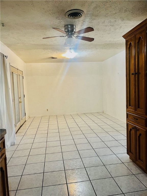 empty room with a textured ceiling, ceiling fan, and light tile patterned floors